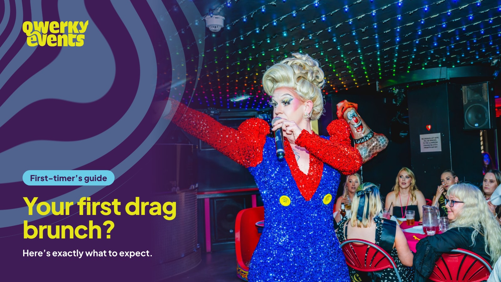 A drag queen in a sparkly blue and red outfit singing to guests at their table